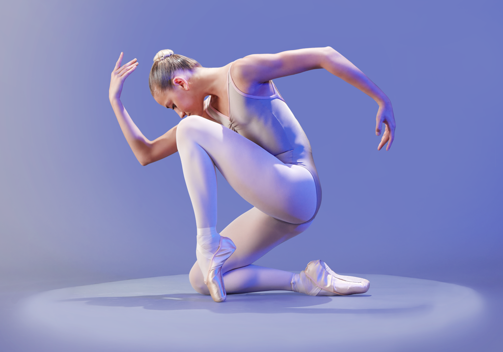 Ballet dancer in nude tights and pointe shoes kneeling on stage