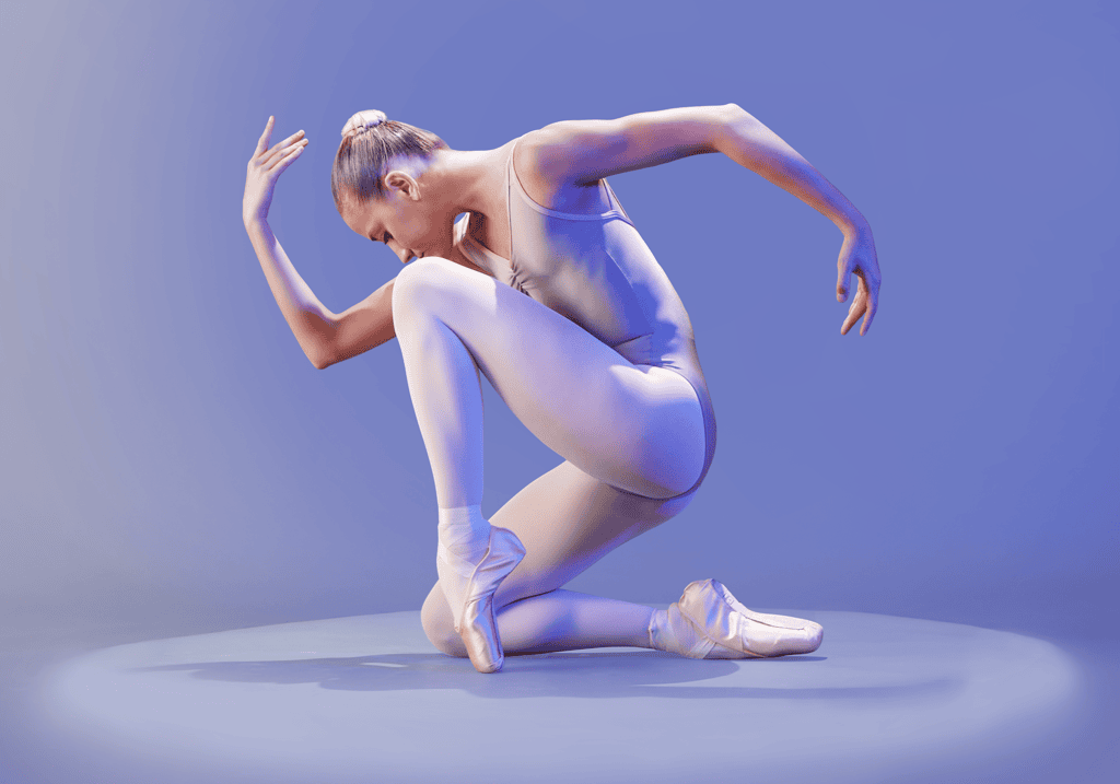 Ballet dancer in nude tights and pointe shoes kneeling on stage